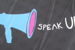 Image of a dark sheet with a blue megaphone and the words Speak Up drawn on it.