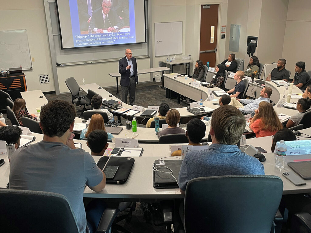 Image of Richard M. Bowen in front of the UTD MBA program with a slide of Citigroup testimony behind him during his talk in 2022.