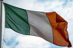 Irish flag against a blue sky with white clouds.