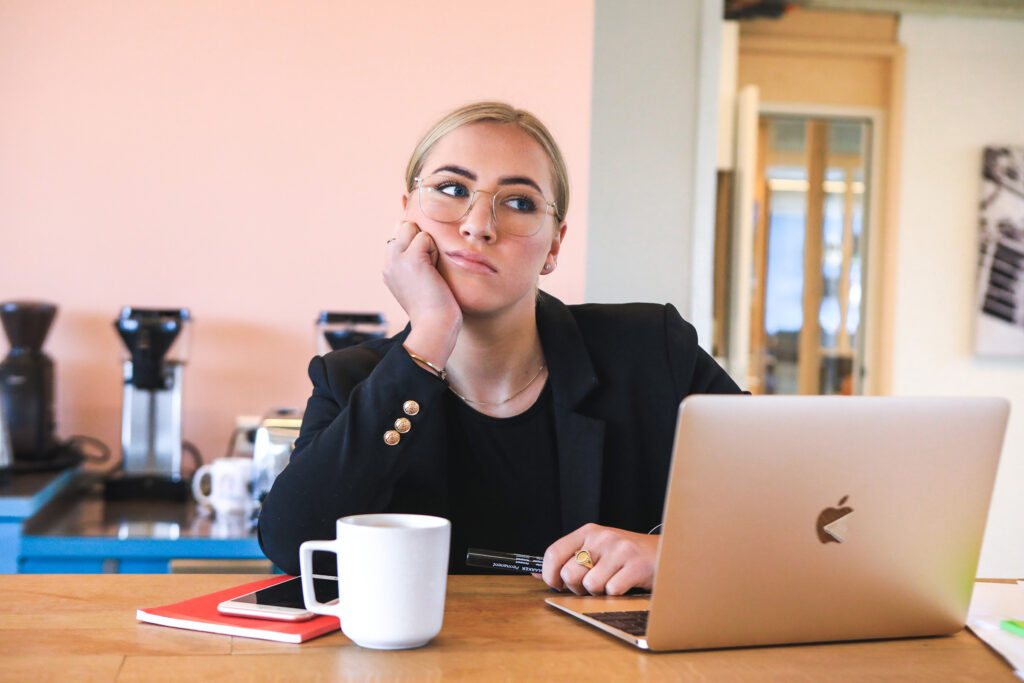 Image of woman in suite leaning face on hand behind open laptop.