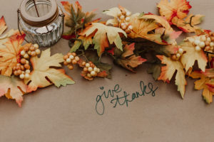 Fall leaves around a candle wiht "give thanks" written on the table